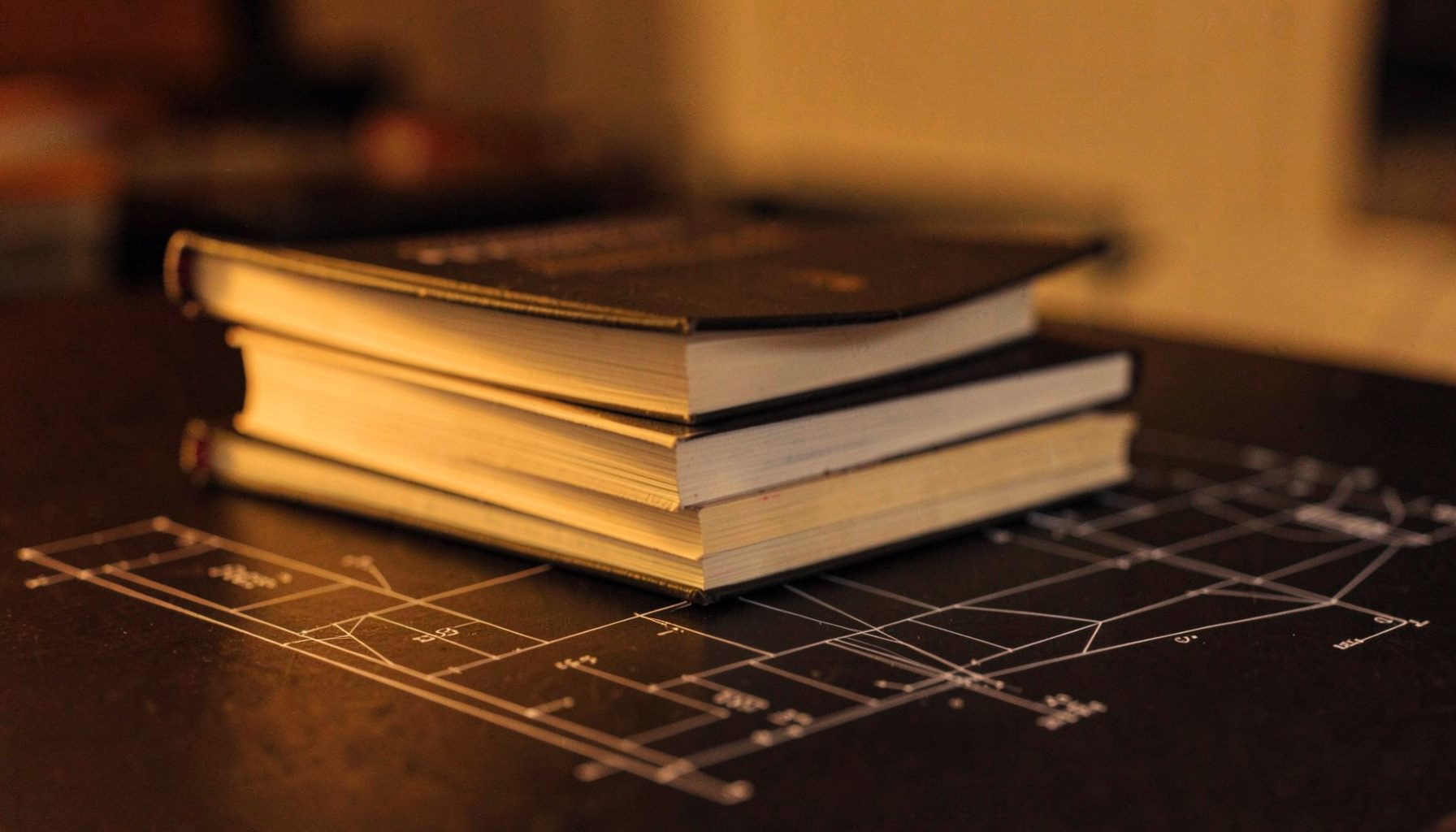 A stack of paperback books on a dark surface lit by warm amber light, spines facing outward in soft focus